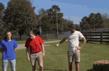 three men are standing in a grassy field with one wearing a white shirt that says ' i love you '