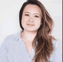 a woman with long hair is wearing a blue and white striped shirt and smiling .