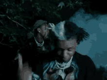 a man with dreadlocks and a skull t-shirt is standing in a dark forest .