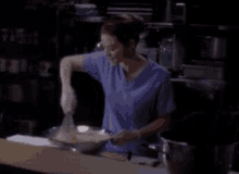 a woman in a blue scrub top is stirring something in a pan