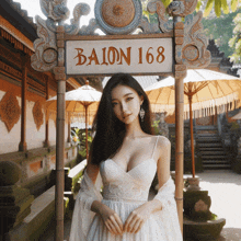 a woman in a white dress stands in front of a sign that reads balon 168