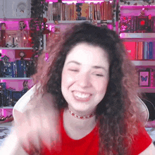 a woman with curly hair wearing a red shirt is smiling in front of a bookshelf with a picture of a butterfly on it