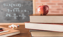 an apple sits on top of a stack of books in front of a chalkboard