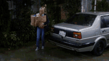 a woman carrying groceries is standing next to a silver car with a license plate that says ' spc1637 '