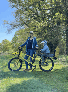 a woman is standing next to a yellow bicycle with a child on the back