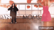 two women dancing in front of a sign that says dance moms