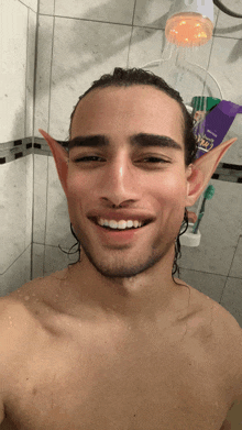 a man with elf ears is smiling in a shower with a bottle of nivea shampoo behind him