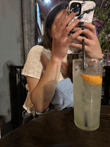 a woman taking a picture of herself with her phone next to a glass of liquid