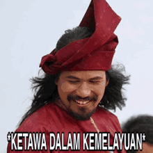 a man with a beard wearing a red shirt and a red turban says ketawa dalam kemaluan *