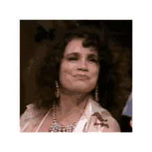 a woman with curly hair is wearing a necklace and earrings and making a funny face .