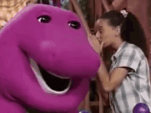 a girl is kissing a purple dinosaur on the cheek .