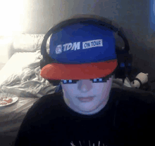 a person wearing headphones and a blue hat that says tdm on tour