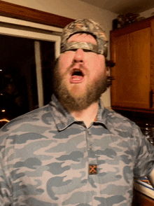 a man with a beard wearing a camo shirt with the letter x on it