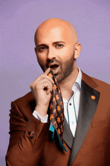 a bald man in a brown suit holds a scarf around his mouth