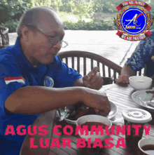 a man in a blue shirt sits at a table with bowls of food and the words agus community luar biasa