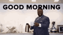 a man in a suit and tie is holding a cup of coffee in front of a wall that says good morning .