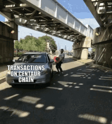 a man is standing under a bridge next to a car with the words transactions on centaur chain written on it .