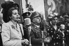 a woman is singing into a microphone while standing in front of a crowd of people in military uniforms .