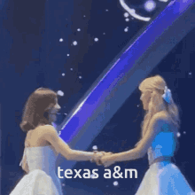 two women in white dresses are shaking hands on a stage with the words texas a & m above them .