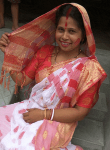 a woman wearing a pink and white dress and a red head scarf smiles