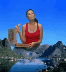 a woman in a red tank top sits on a mountain eating pizza