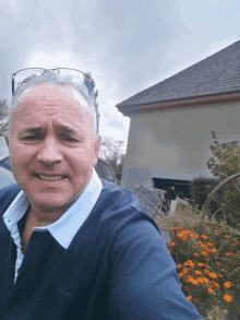 a man wearing glasses and a blue sweater stands in front of a house