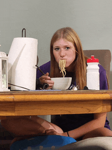 a girl is sitting at a table eating noodles with a spoon