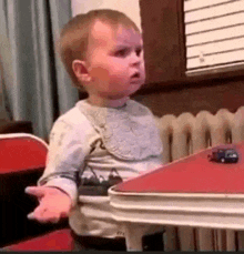 a baby is sitting at a red table with a toy car on it .