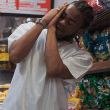 a man in a white shirt holds his head while standing in front of a shelf with a bag of rice on it