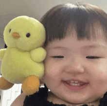 a baby is holding a stuffed yellow chicken and smiling