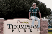 a man is sitting on a sign for thompson park