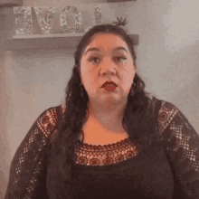 a woman in a black lace top is standing in front of a shelf with the word love on it