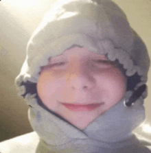 a young boy wearing a hooded sweatshirt and a hat is smiling with his eyes closed .