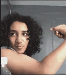 a young man with curly hair is flexing his muscles in front of a bottle of water