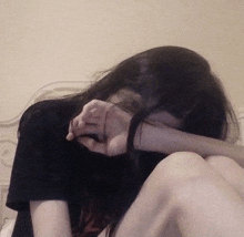 a girl is sitting on a bed covering her face with her hand .