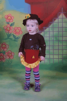 a little girl wearing a hat and apron is standing in front of flowers