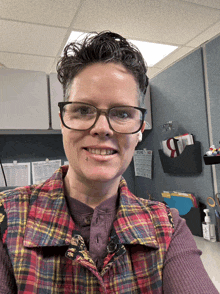 a woman wearing glasses and a plaid shirt smiles in front of a calendar that says ' october ' on it