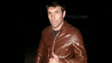 a man in a brown leather jacket stands in the dark