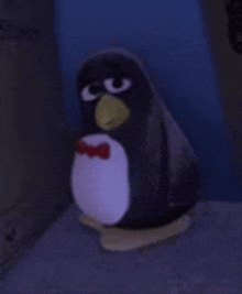 a stuffed penguin with a red bow tie is sitting on a table in a dark room .