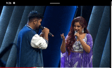 a man singing into a microphone next to a woman with a purple dress