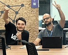 a man wearing a vans shirt is sitting at a desk with another man