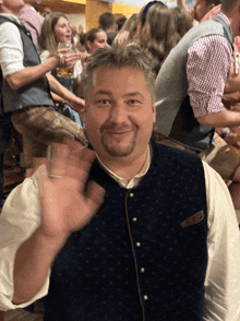 a man in a blue vest is smiling and waving in a crowd