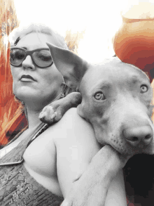 a woman with glasses holds a dog on her shoulders