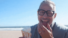 a man with glasses is eating ice cream on the beach .