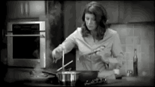 a black and white photo of a woman cooking in a kitchen with steam coming out of the pot .