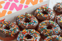 a box of chocolate donuts with sprinkles sits on a table