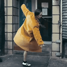 a woman in a yellow coat is dancing in front of a building with a sign on the door that says police department