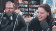 a man and a woman are smiling in front of microphones in a room with stuffed animals on the shelves