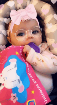 a baby wearing glasses and a pink headband holds a pink bag that says " unicorns are real "