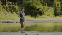 a man in a blue shirt is standing in a body of water with a national geographic logo in the background